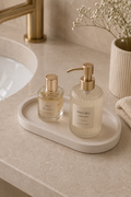 Minimalist oval vanity tray in soft white with luxury perfume bottle, gold bracelet and ring on a travertine stone table, neutral home decor by Odyssey Interior
