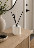 Handmade ribbed reed diffuser holder with glass bottle in white styled on a modern entryway console table with neutral home decor.